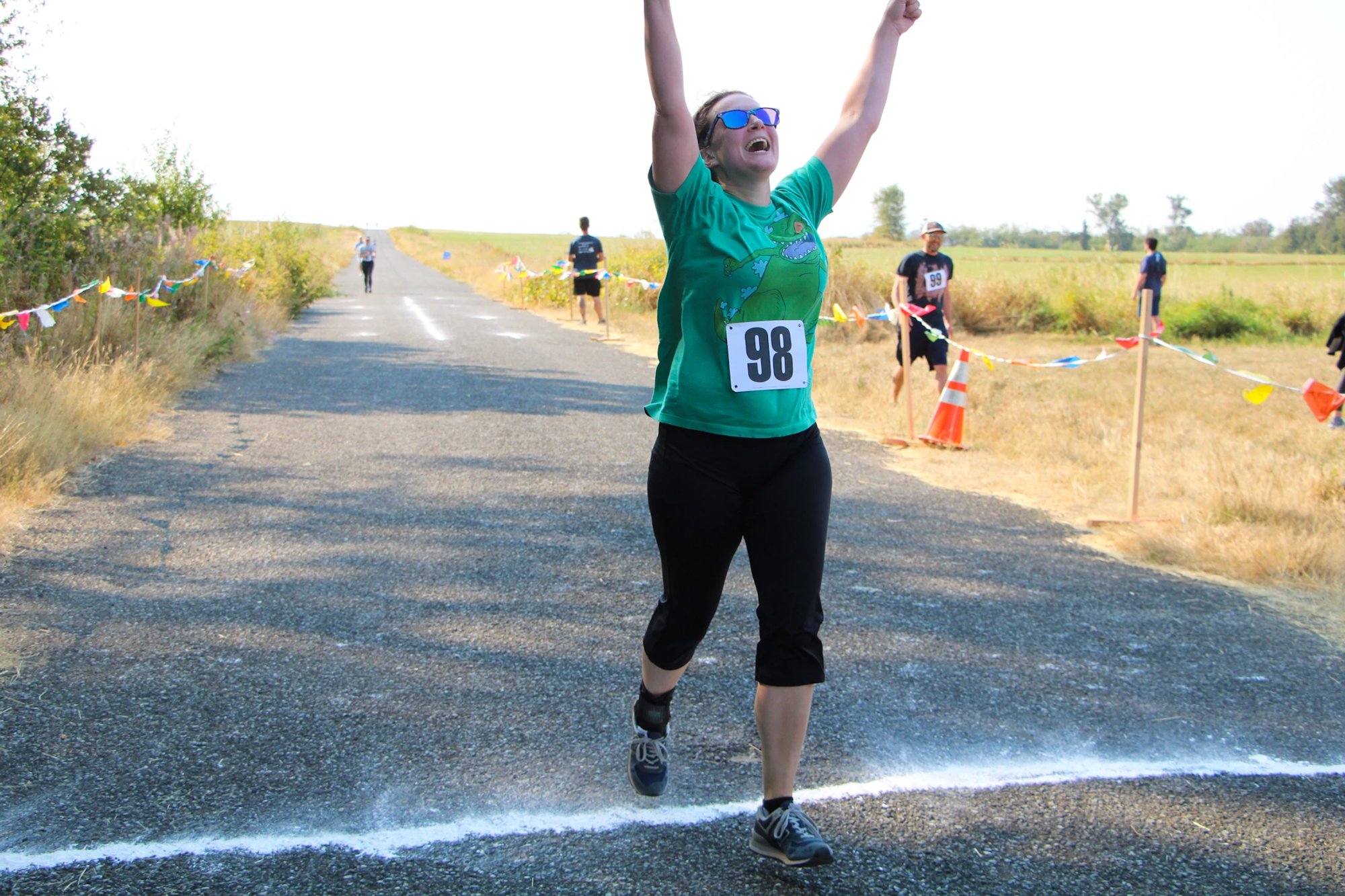 Runner crossing the finish line with arms raised, wearing a green shirt and number 98.