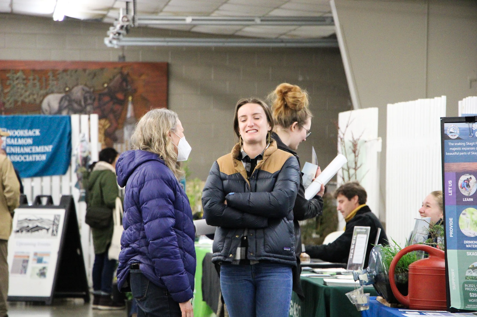 People interacting at an indoor event with informational tables and banners.