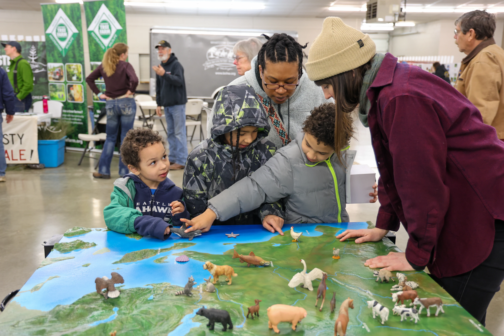 People examining a 3D map with animal figures at an indoor event.