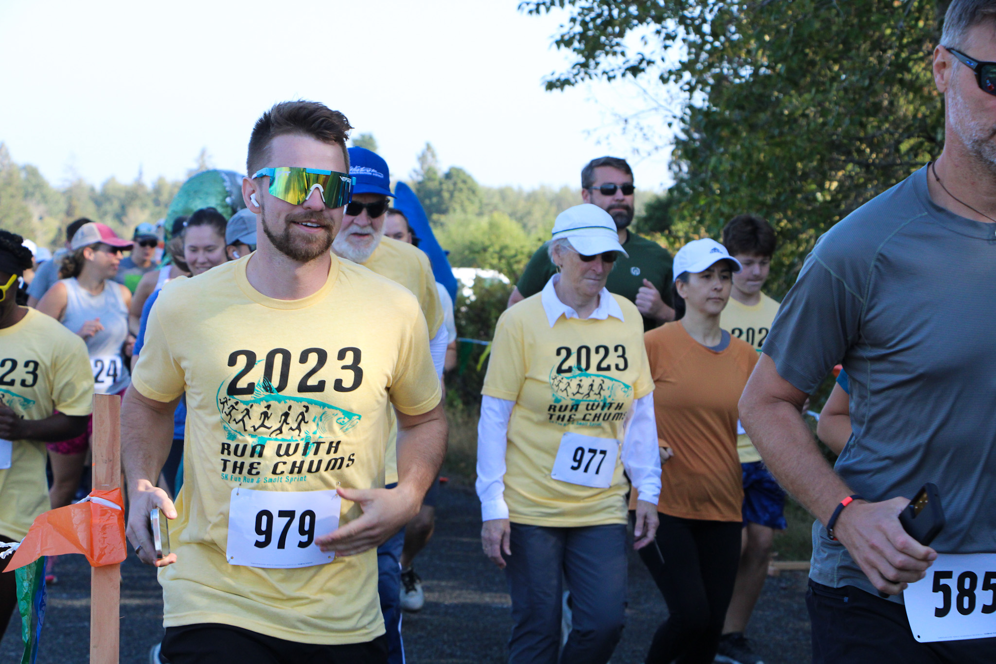 People running in a race, wearing "2023 Run with the Chums" T-shirts, outdoors with trees in the background.
