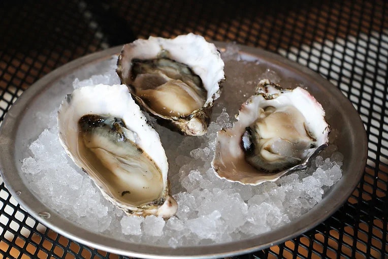 Three raw oysters on a bed of ice in a metal dish.
