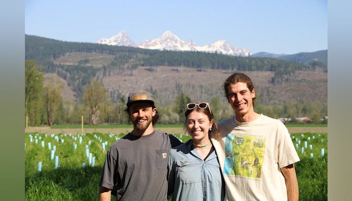 Three people smiling in a field with mountains in the background.
