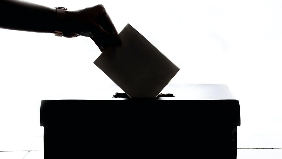 Silhouette of a hand casting a vote into a ballot box.