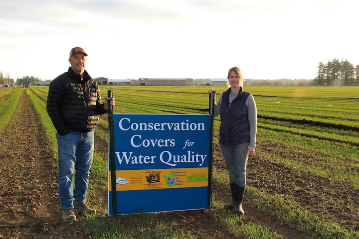 Two people in a field with a sign reading "Conservation Covers for Water Quality."