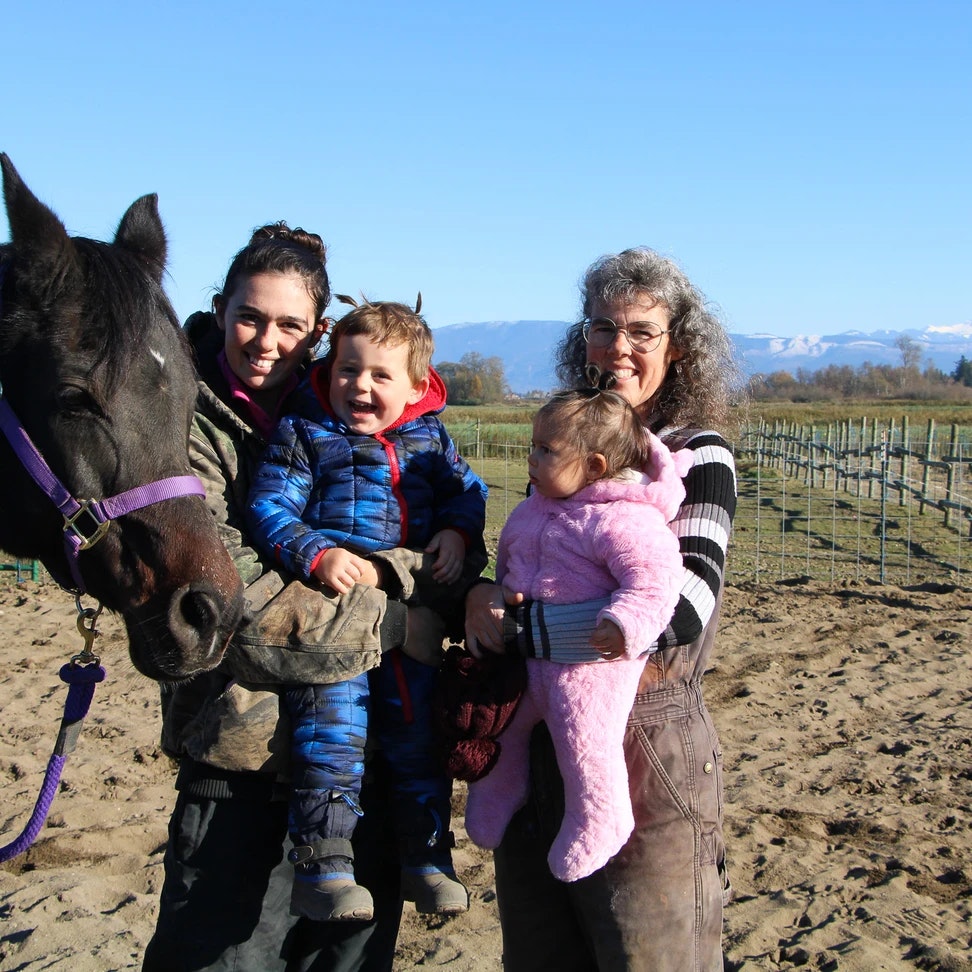 Three people and two children with a horse in a field, under a clear sky.