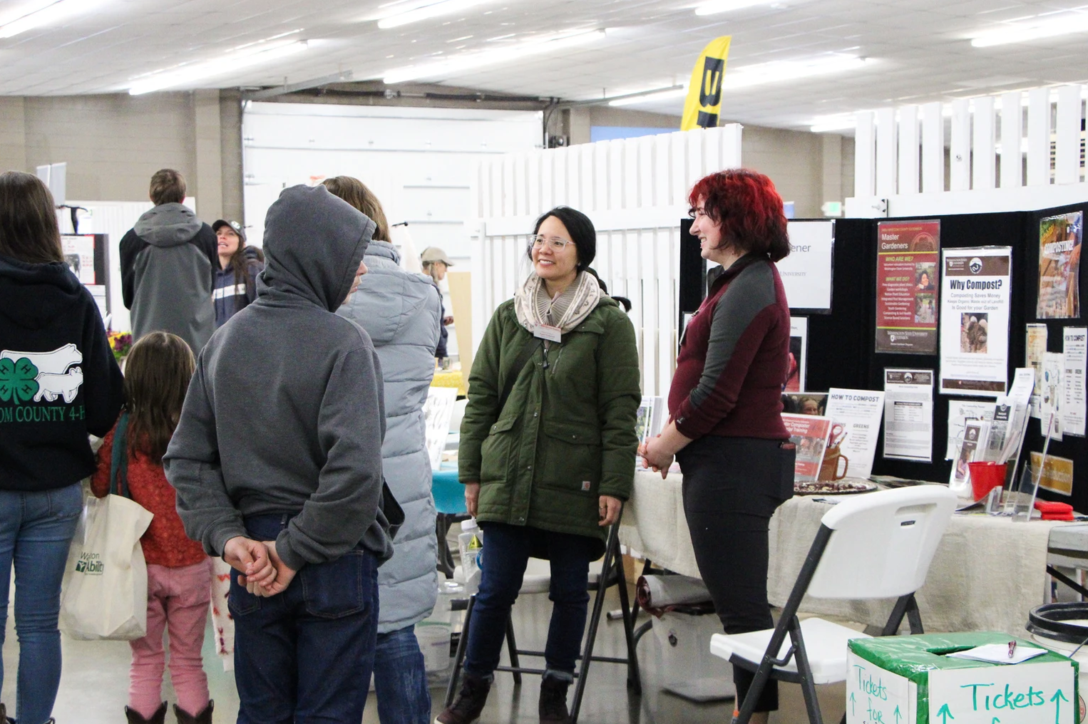 People interacting at an indoor event with informational displays and tickets box visible.
