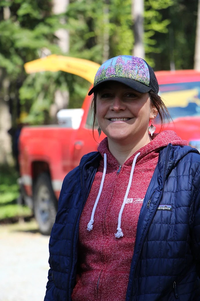 A smiling person wearing a colorful hat and jacket, standing outdoors in front of a red truck.