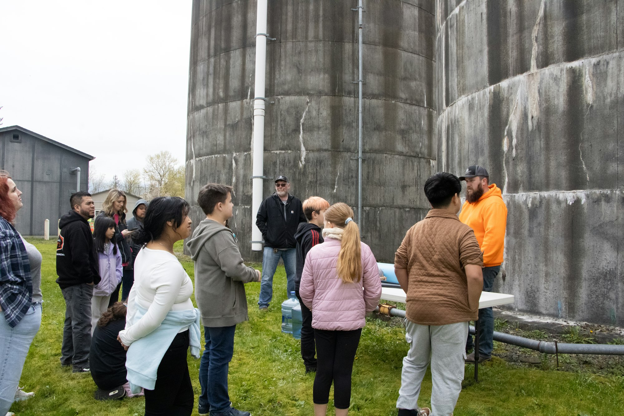A group of people gathered outside, listening to a speaker near large concrete structures, likely on a tour or educational visit.