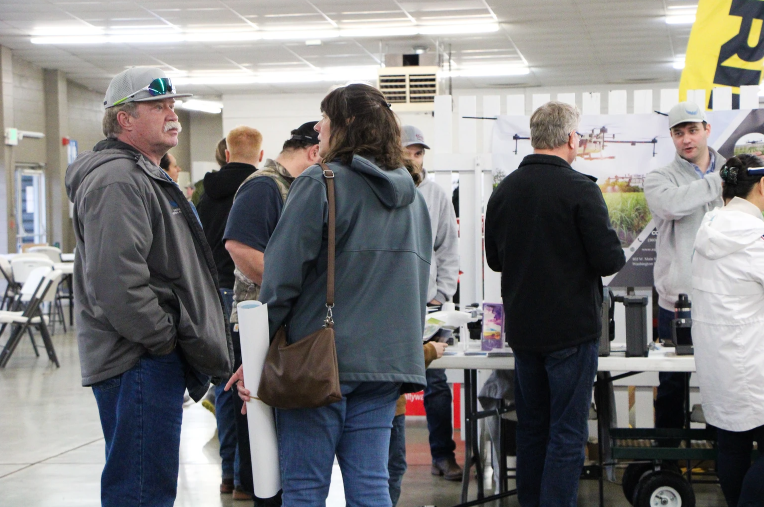 A group of people interacting at an indoor event or conference, with posters and equipment on display.