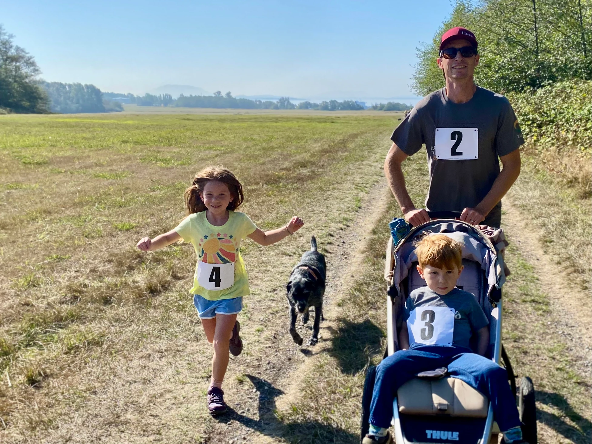 A man, child, and dog on a countryside trail; man pushing a stroller with a seated toddler.