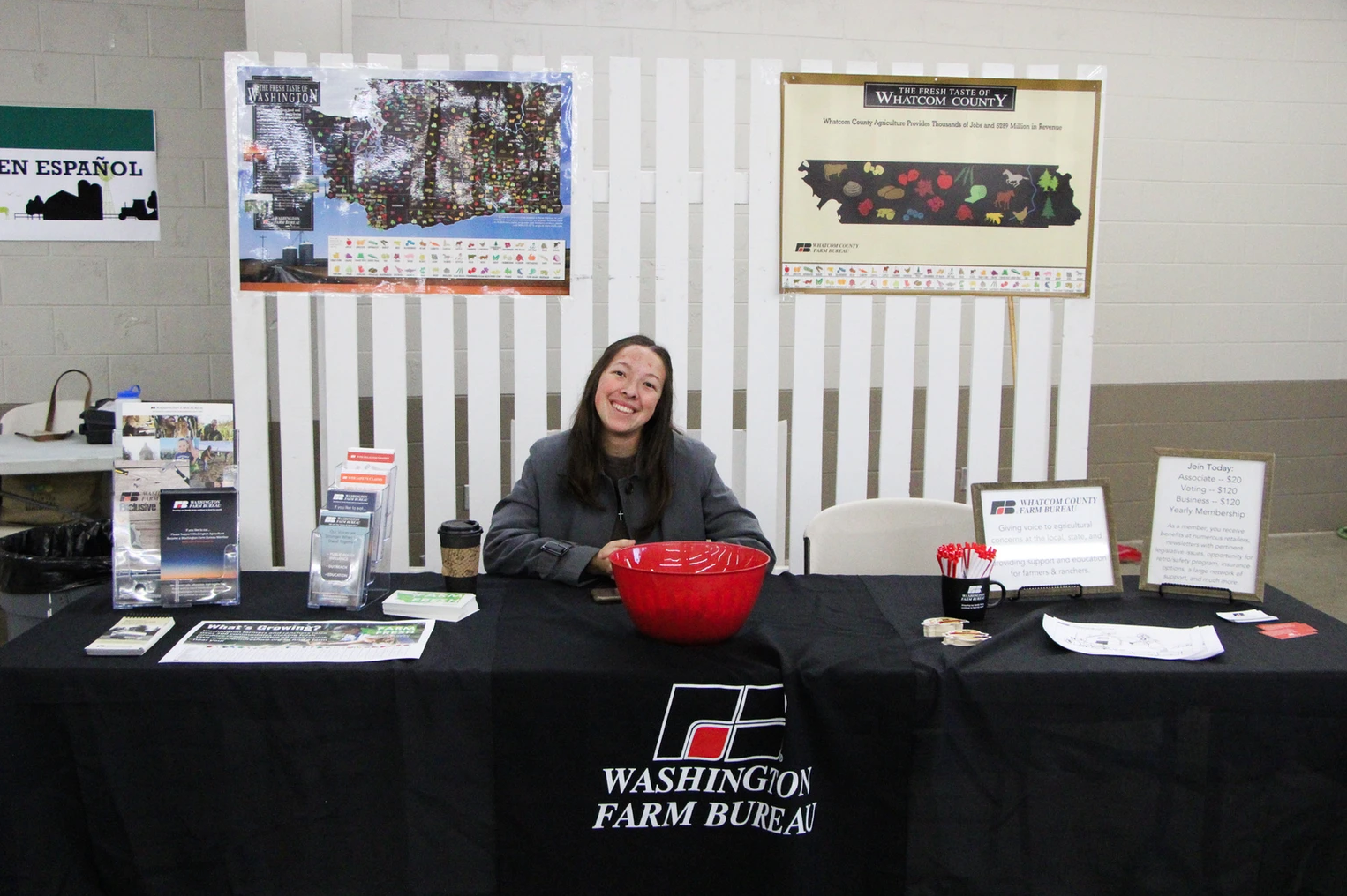 A woman at a Washington Farm Bureau booth with maps, brochures, a red bowl, and a display promoting agricultural information.