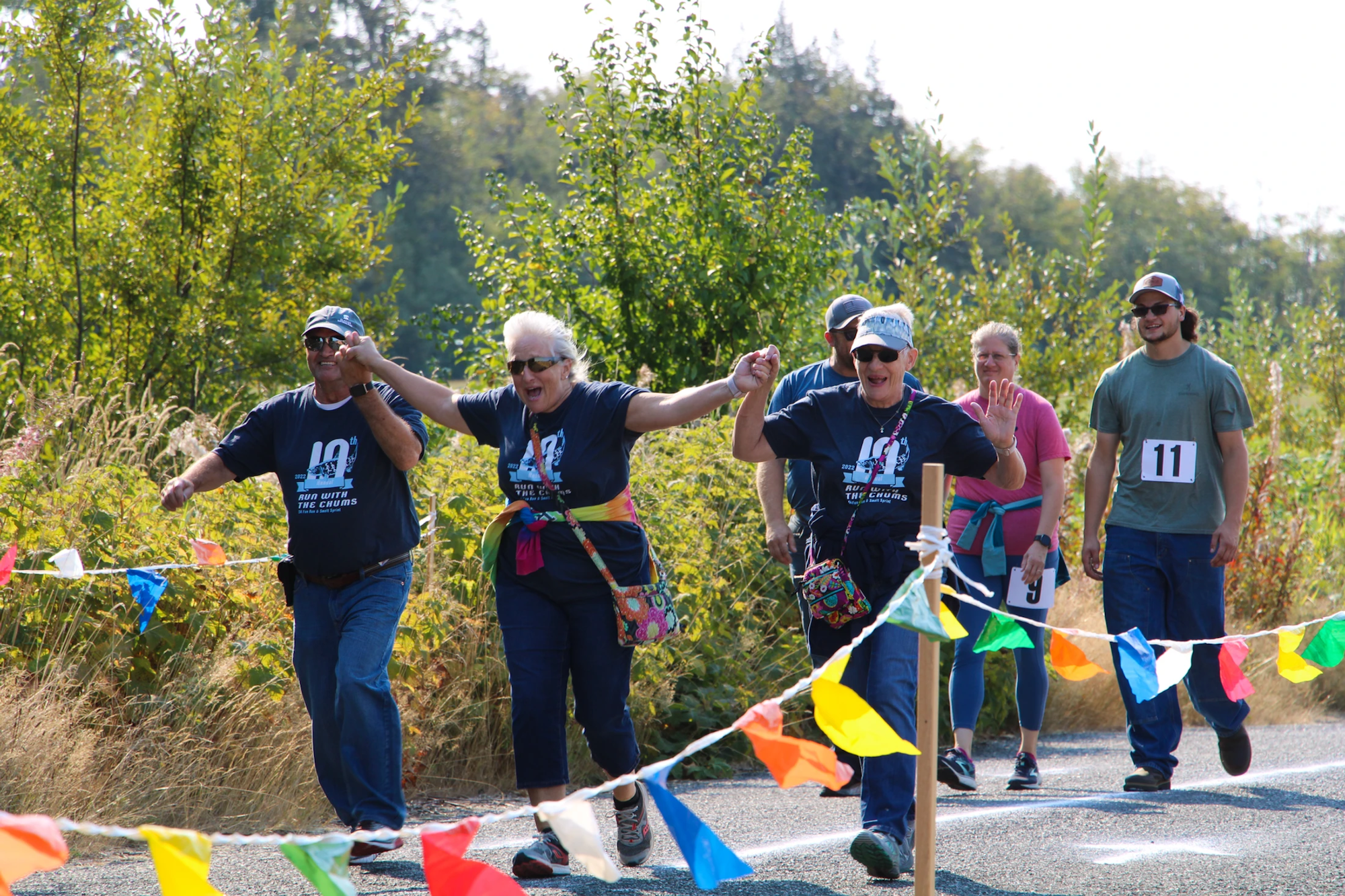 A group of people walking in a joyful outdoor event, with colorful flags and number tags.