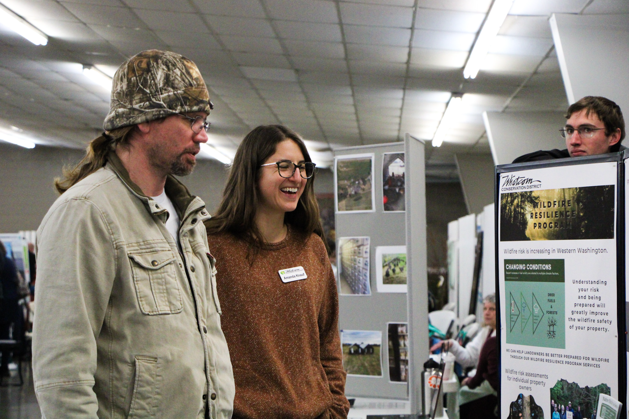 Two people are at an event displaying a "Wildfire Resilience Program" poster.