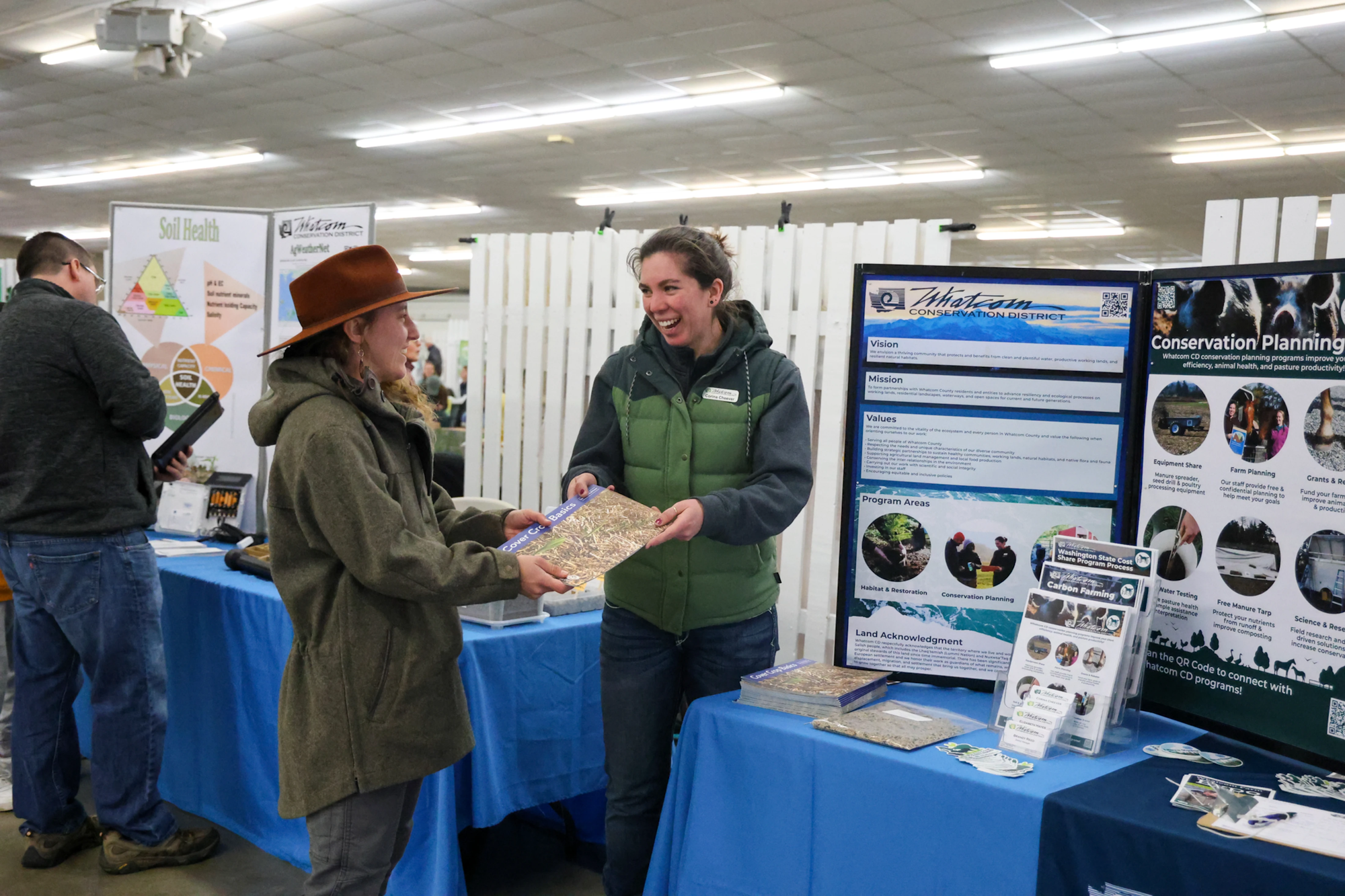 Two people at a conservation booth exchanging materials, with informational posters in the background.