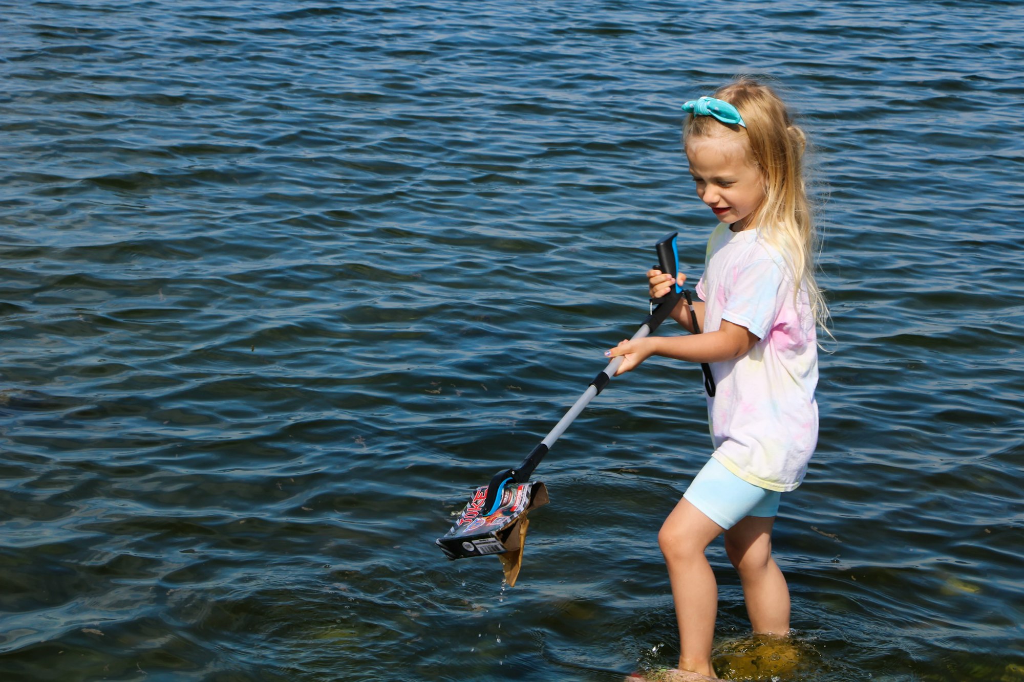 A child uses a grabber tool to pick up trash from the water.