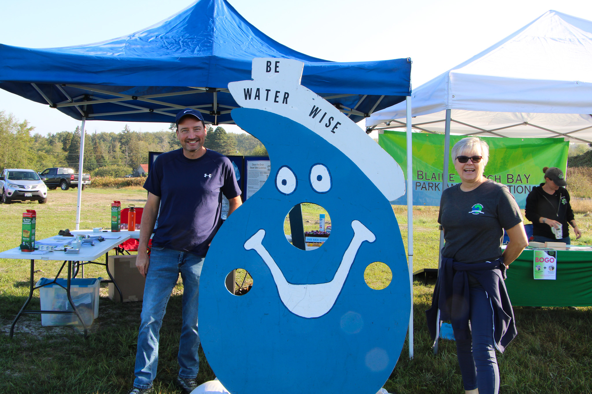 People smiling next to a blue "Be Water Wise" character cutout at an outdoor event.