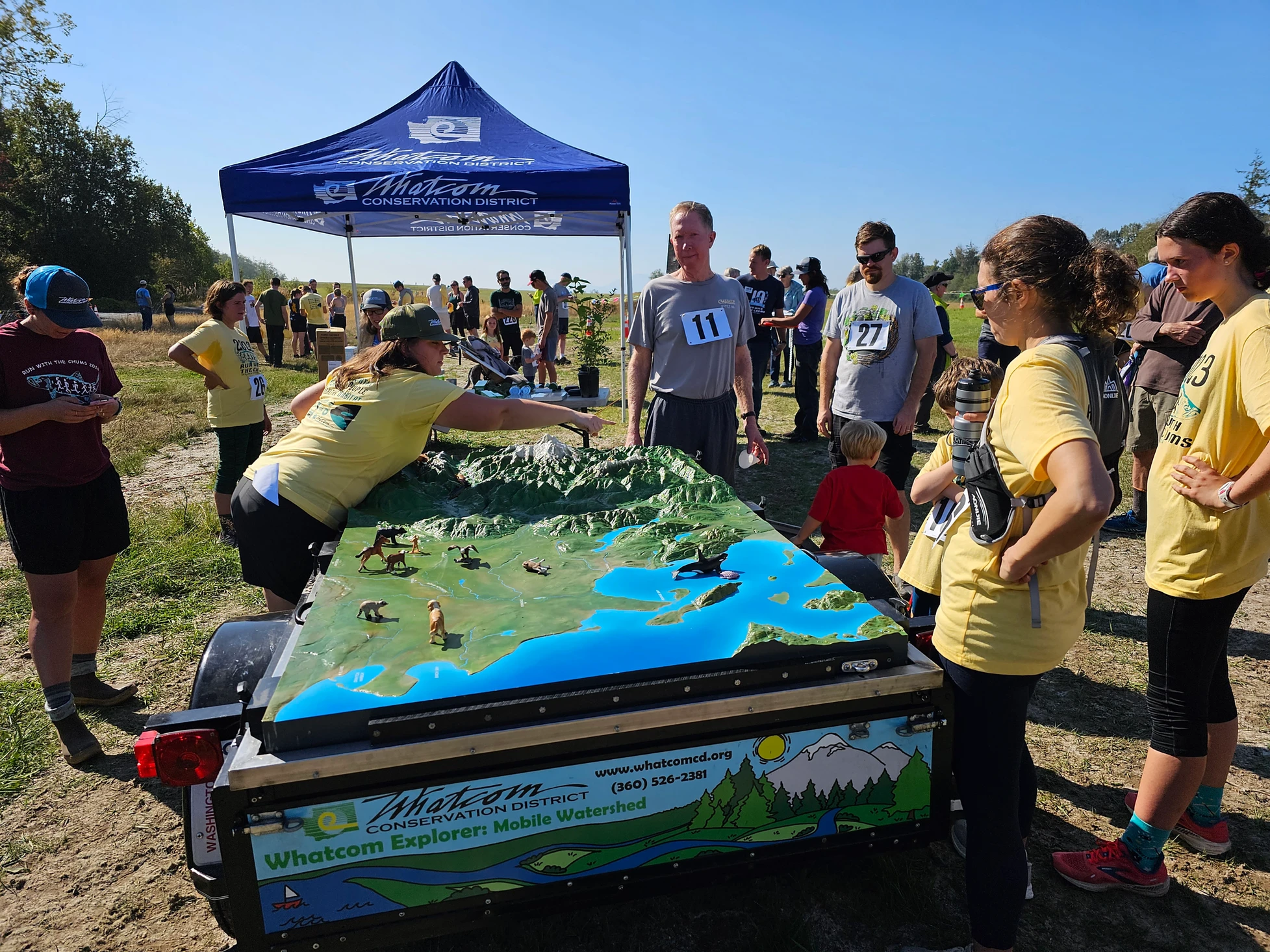People gathered around a mobile watershed model under a Whatcom Conservation District tent.