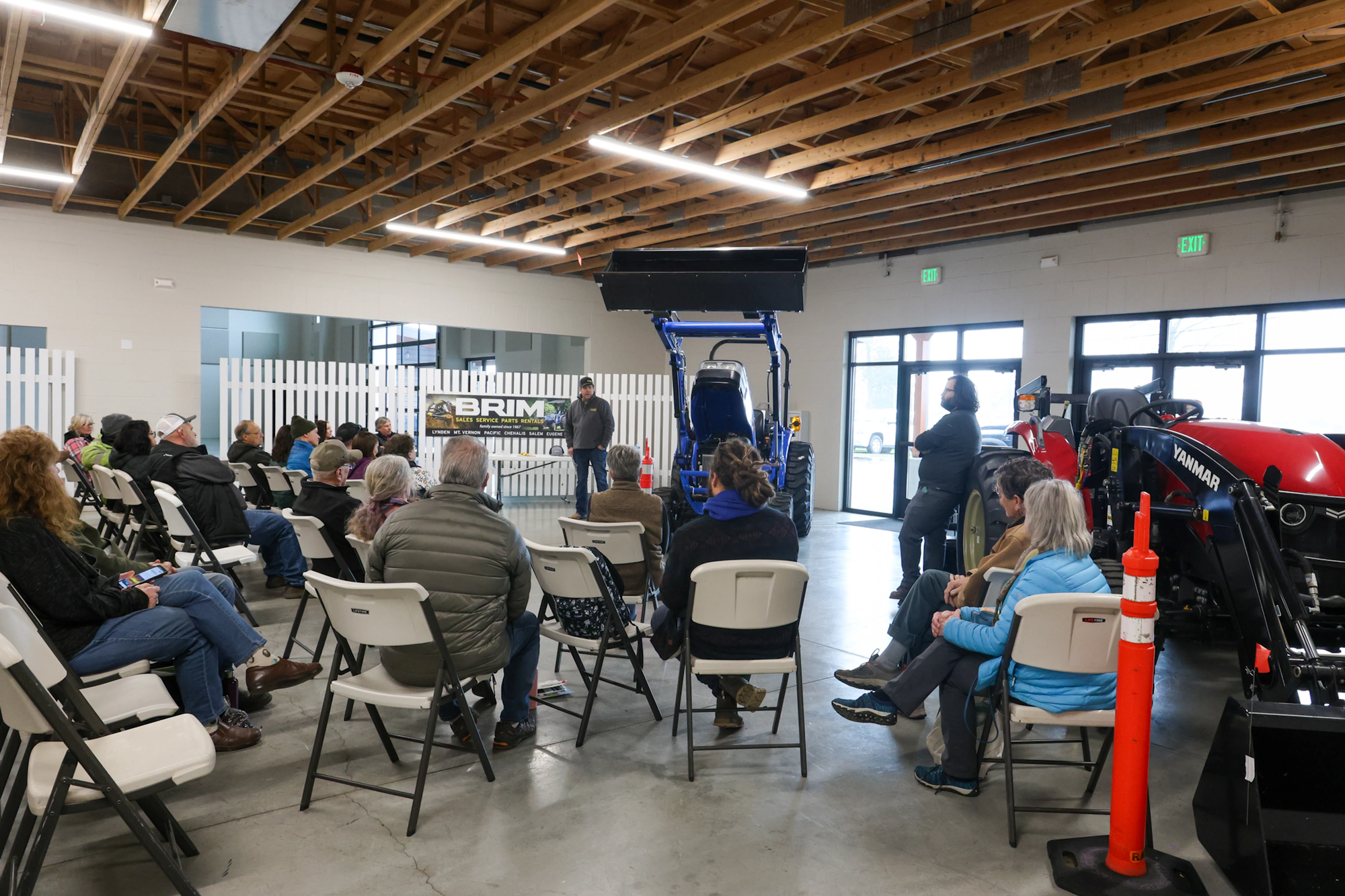 People sitting on chairs indoors, attending a presentation featuring tractors.
