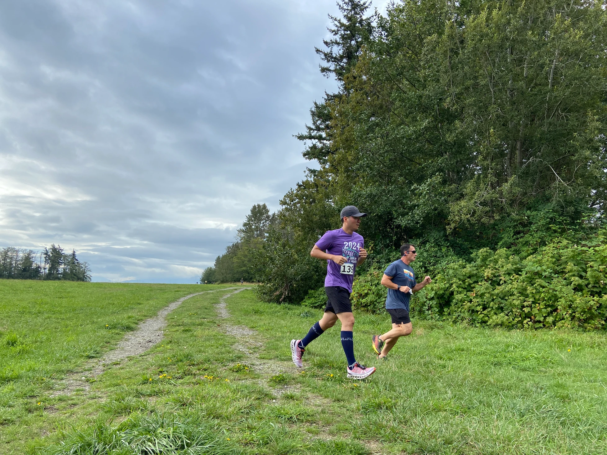 Two people running on a grassy path near trees, with race numbers 139 and 132.