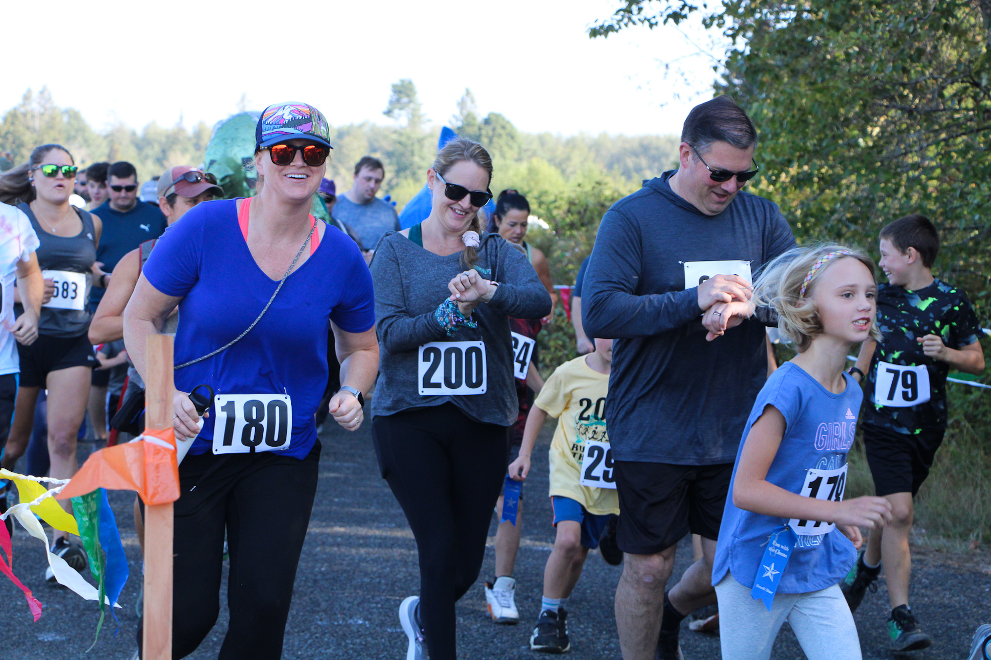 A diverse group of people participating in a fun run or race outdoors, wearing numbered bibs.