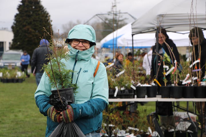 Person in a raincoat holding a plant at an outdoor plant sale with others in the background.