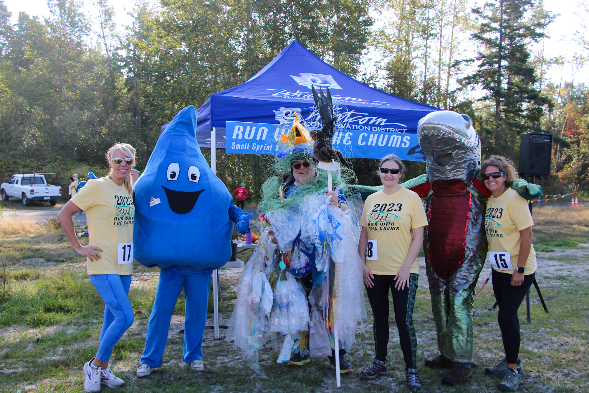 People in costumes and event shirts posing under a "Run With The Chums" tent.