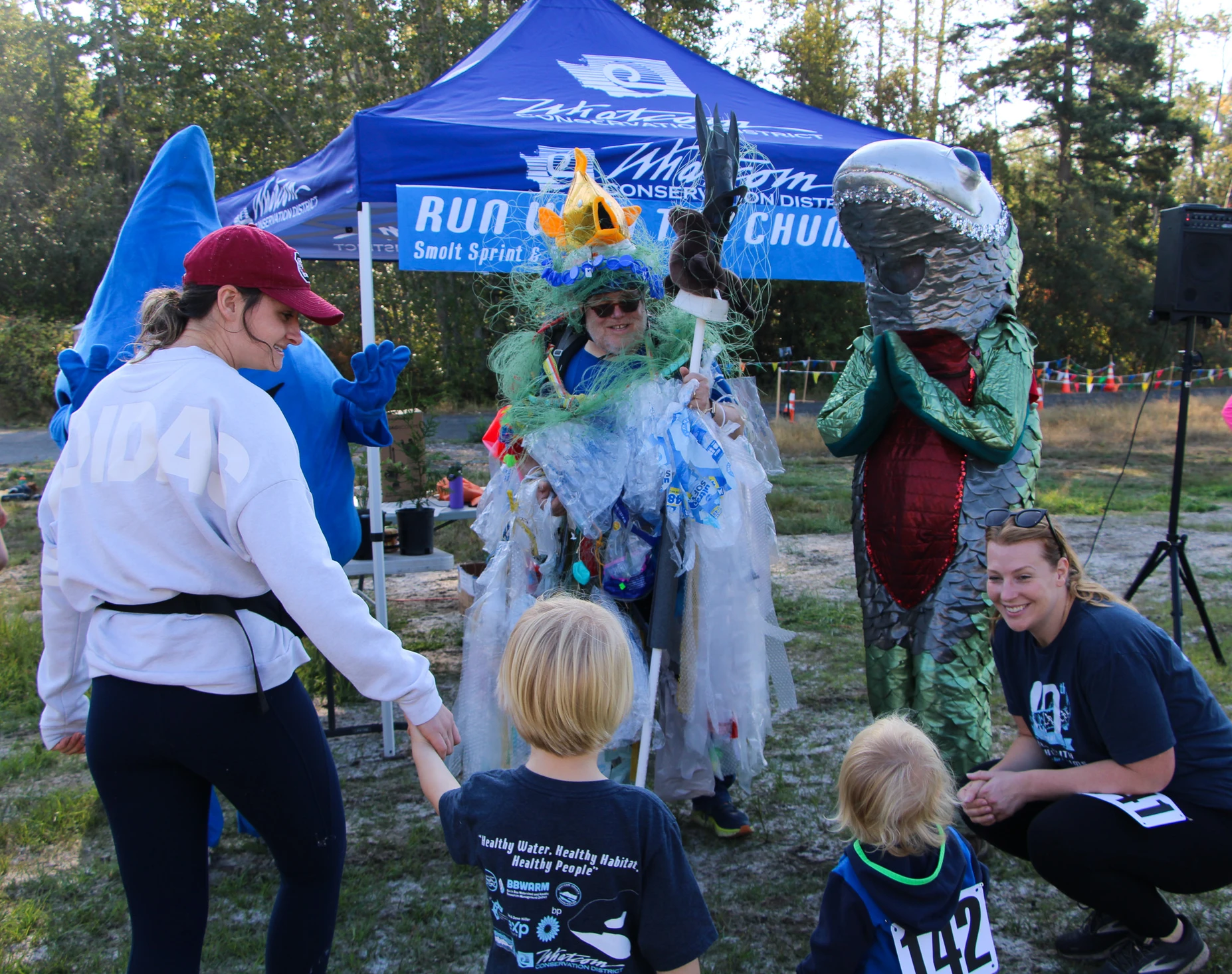 Children meet costumed characters at an outdoor event, under a blue tent.