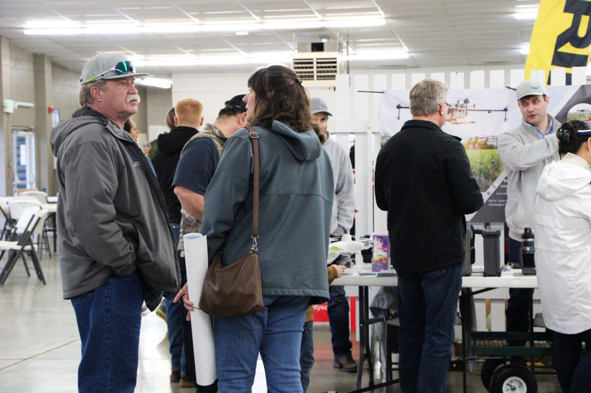 People at an indoor event or expo, engaging in conversations and viewing exhibits.