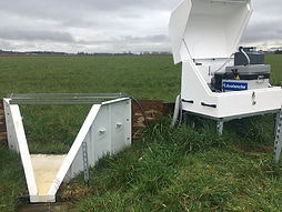 A weather station with an open container and equipment box, set in a grassy field.