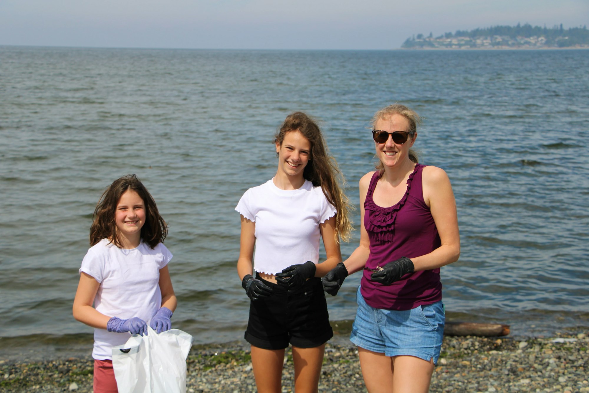 Three people wearing gloves, standing on a beach, possibly collecting trash.