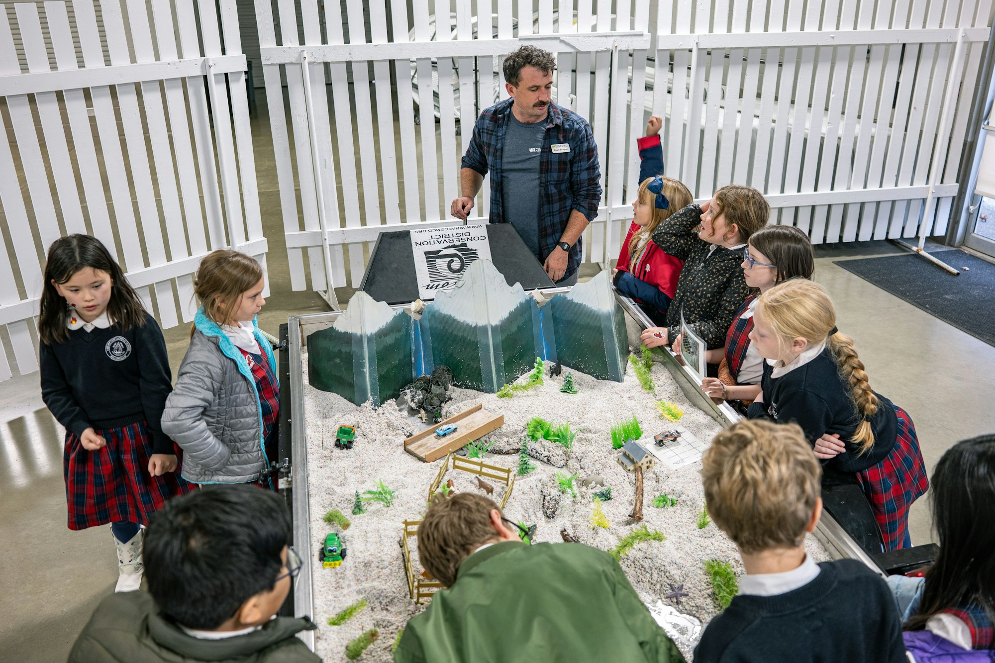Kids are engaged in a hands-on learning activity about conservation, exploring a model landscape with a facilitator.