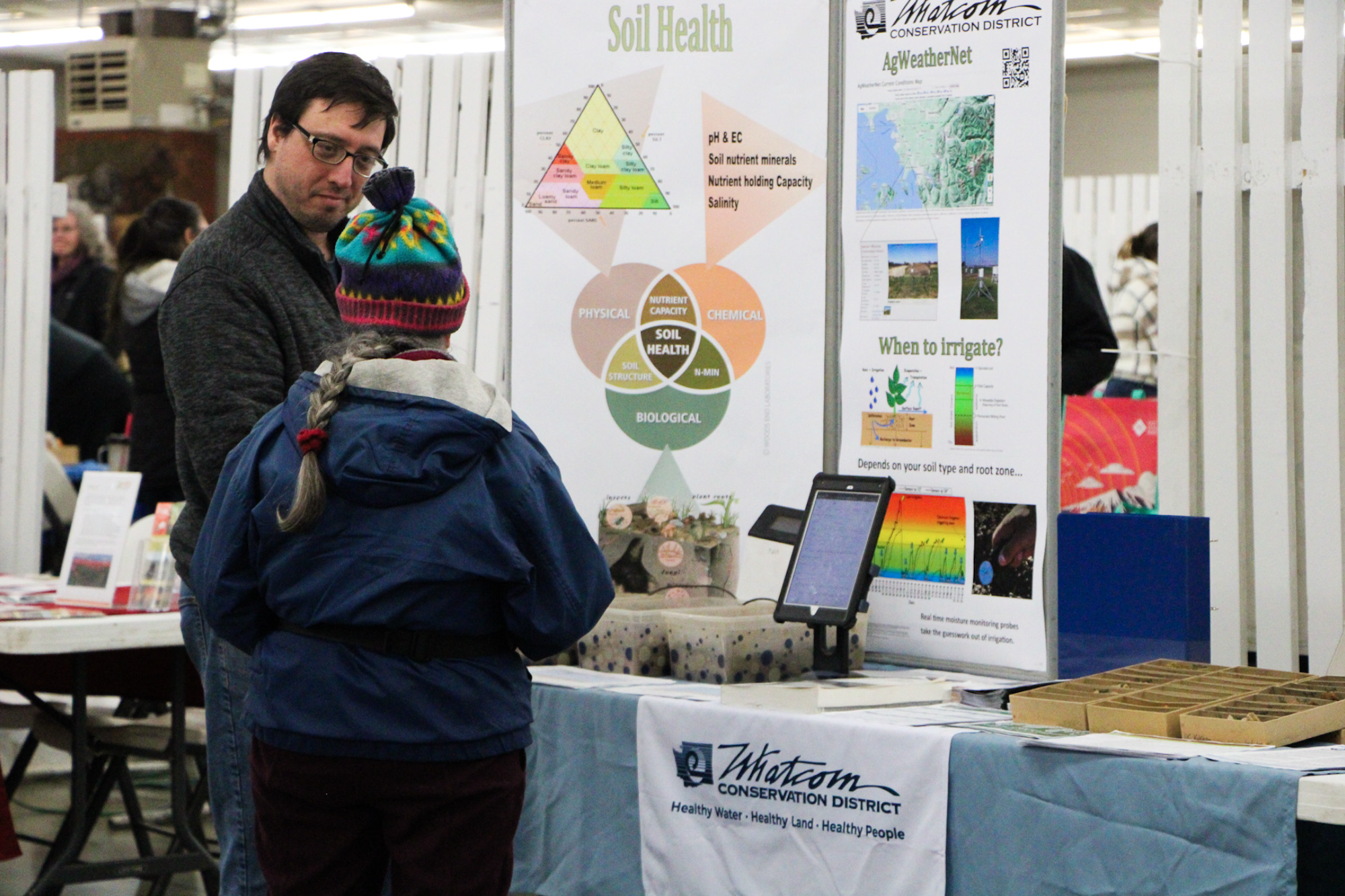 Two people at a conservation booth discussing soil health and irrigation, featuring informational posters and a display.