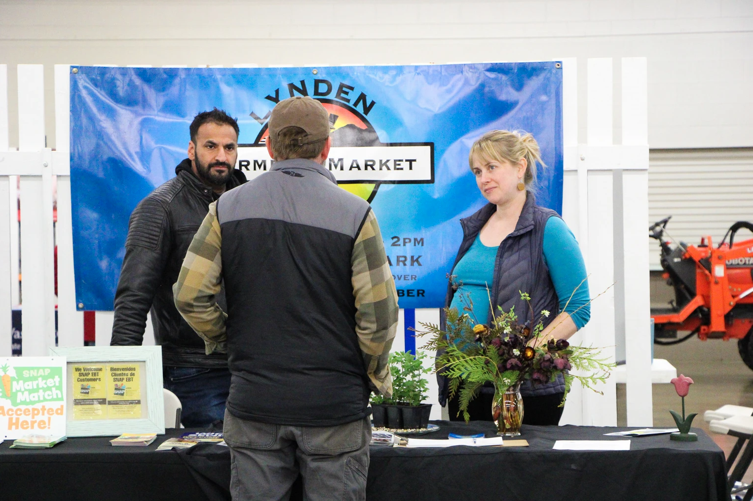 People at a farmers market booth with a "SNAP Market Match Accepted Here" sign.