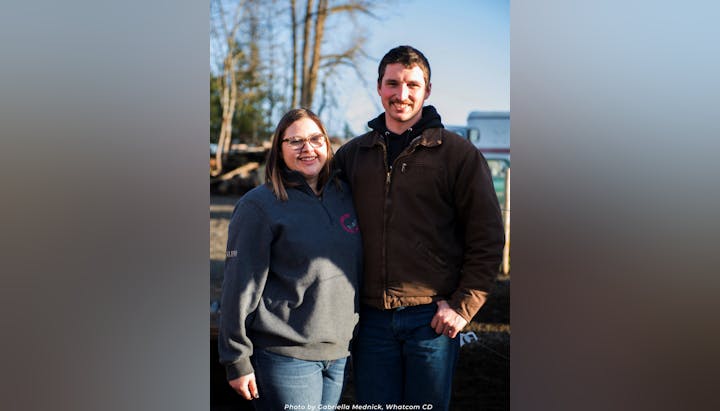 A smiling couple standing outdoors, wearing casual jackets.