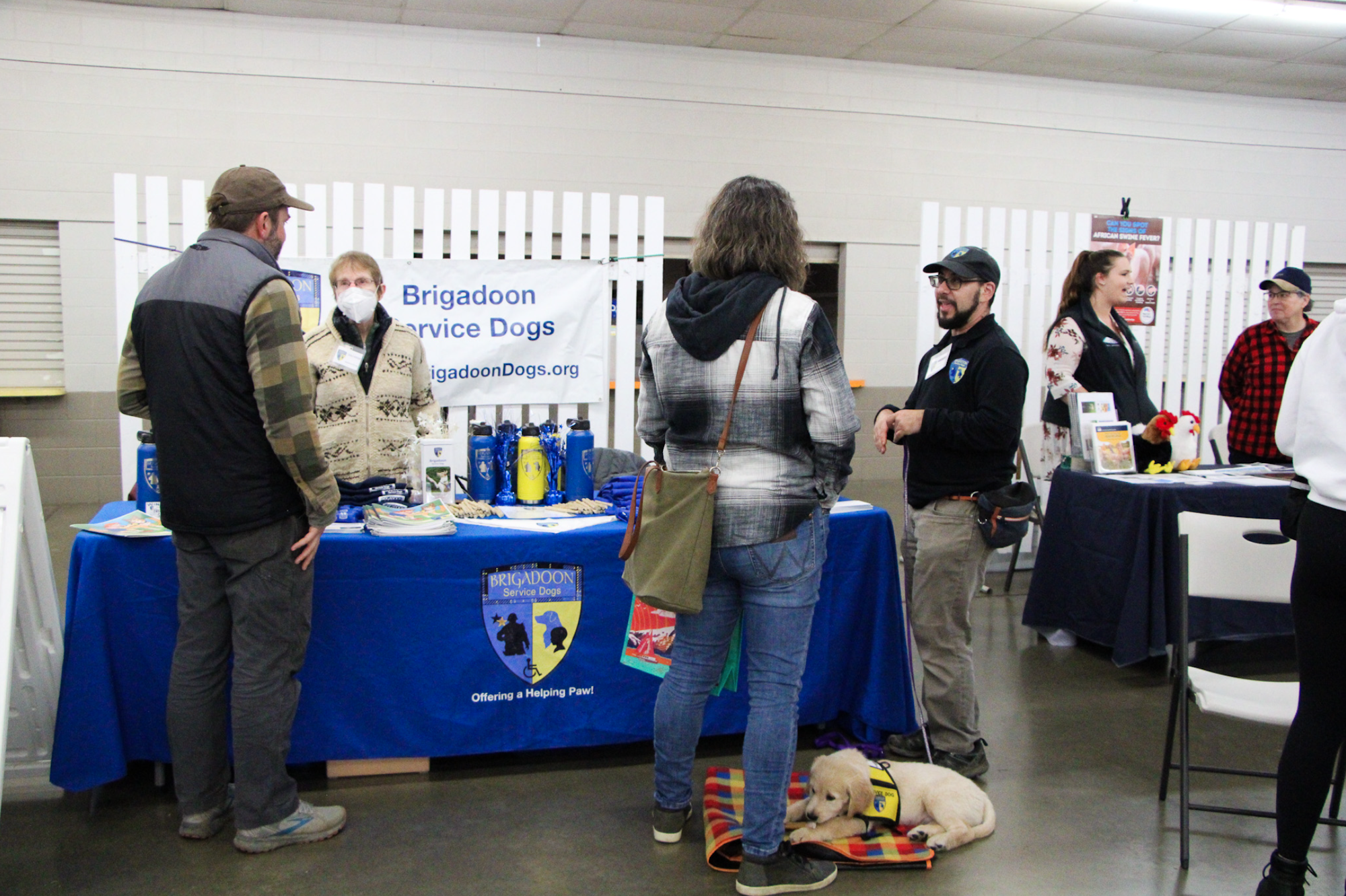 A group of people at a booth for Brigadoon Service Dogs with a puppy laying on a mat.