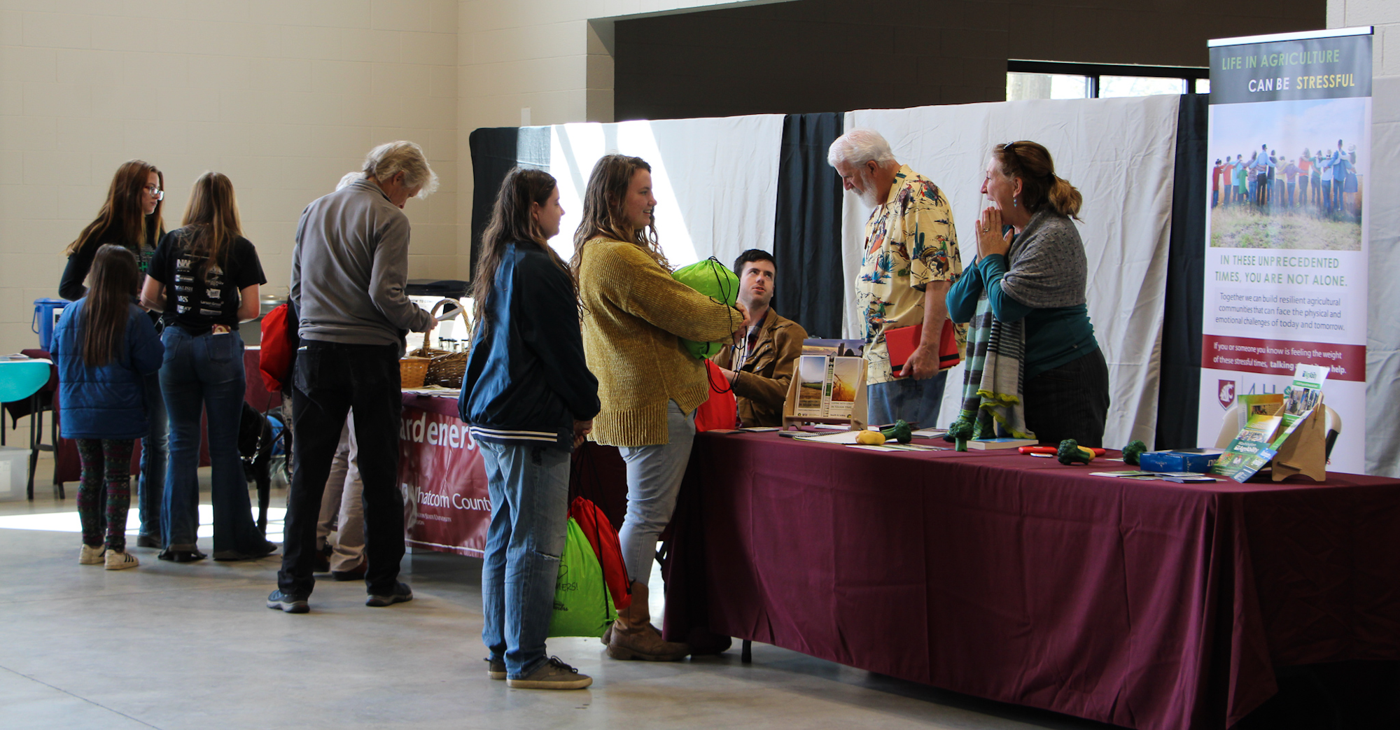People gathered at informational booths with displays and a poster about stress in agriculture settings.