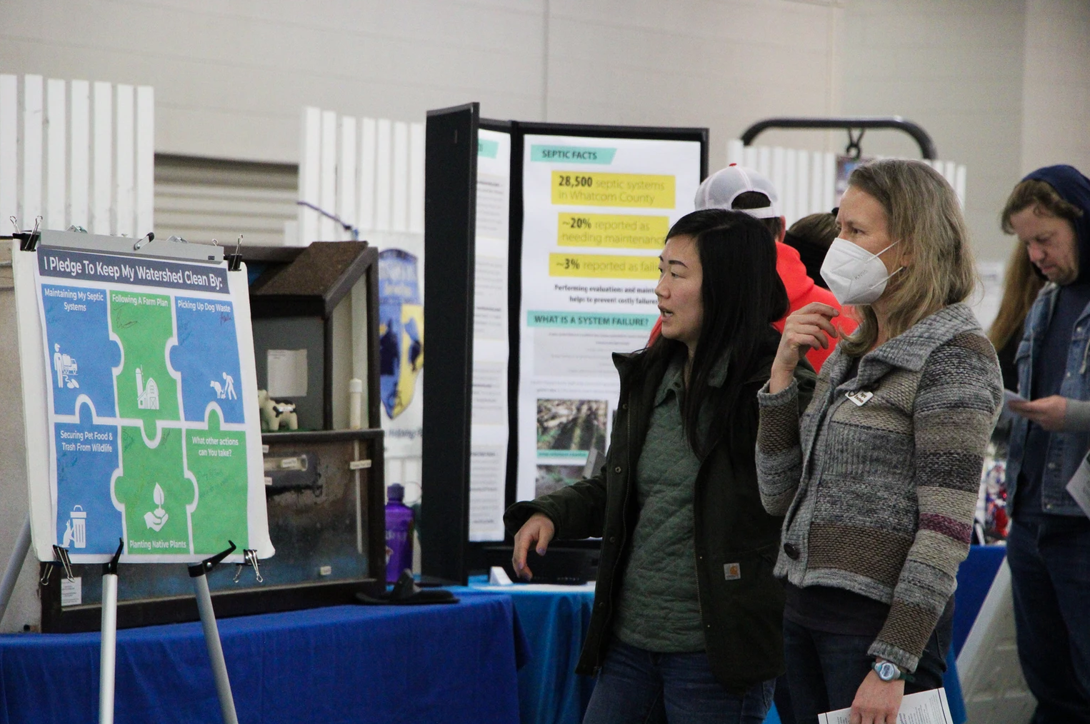 Two people looking at an environmental display about keeping watersheds clean, with informational posters in the background.