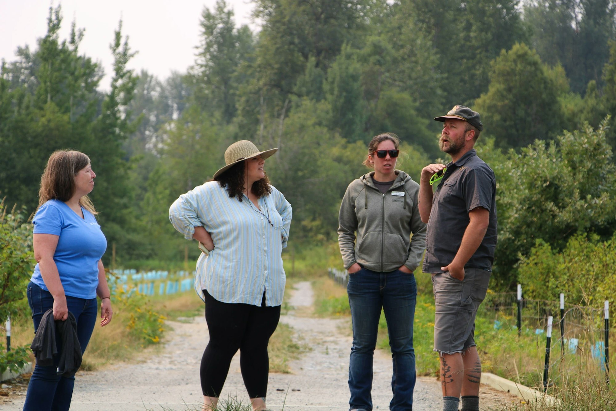 Four people conversing on a dirt path surrounded by trees and greenery.