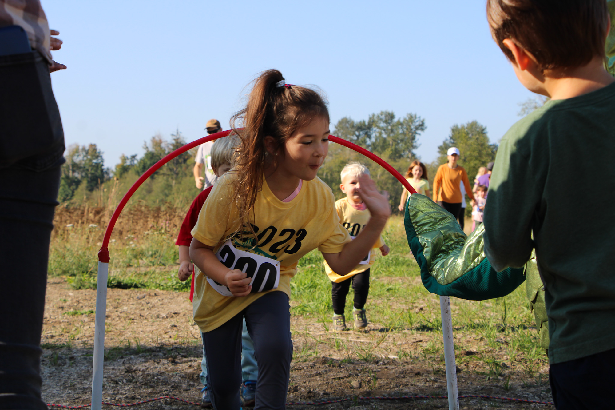 Children running through an obstacle course outdoors, wearing numbered yellow shirts.