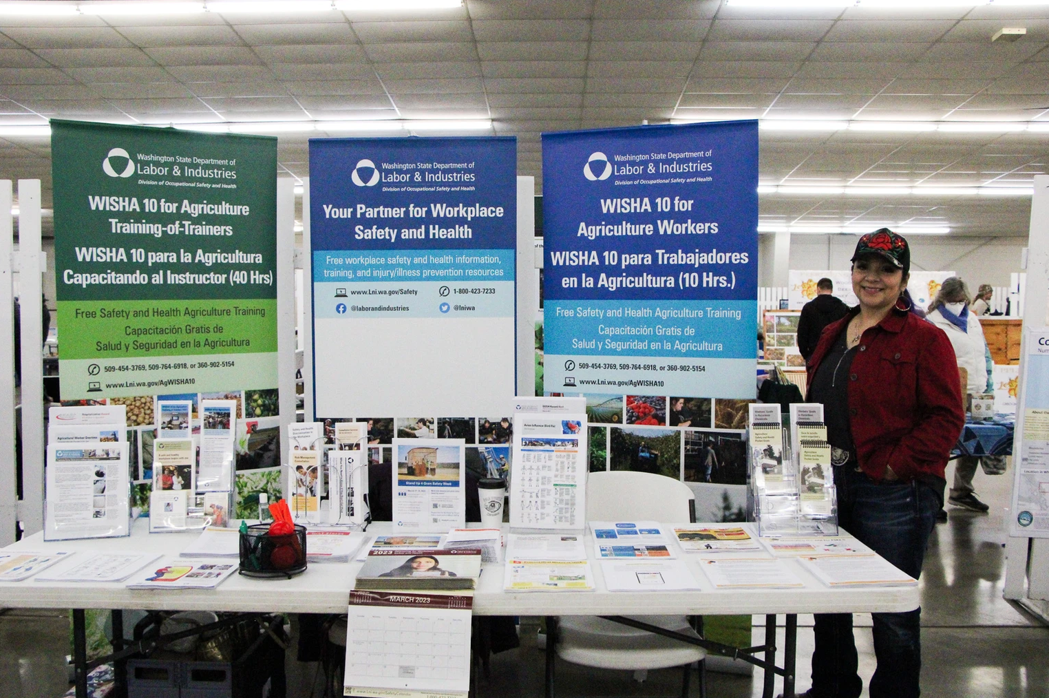 Booth promoting WISHA safety training for agriculture workers by Washington State Labor & Industries with brochures and a smiling person.