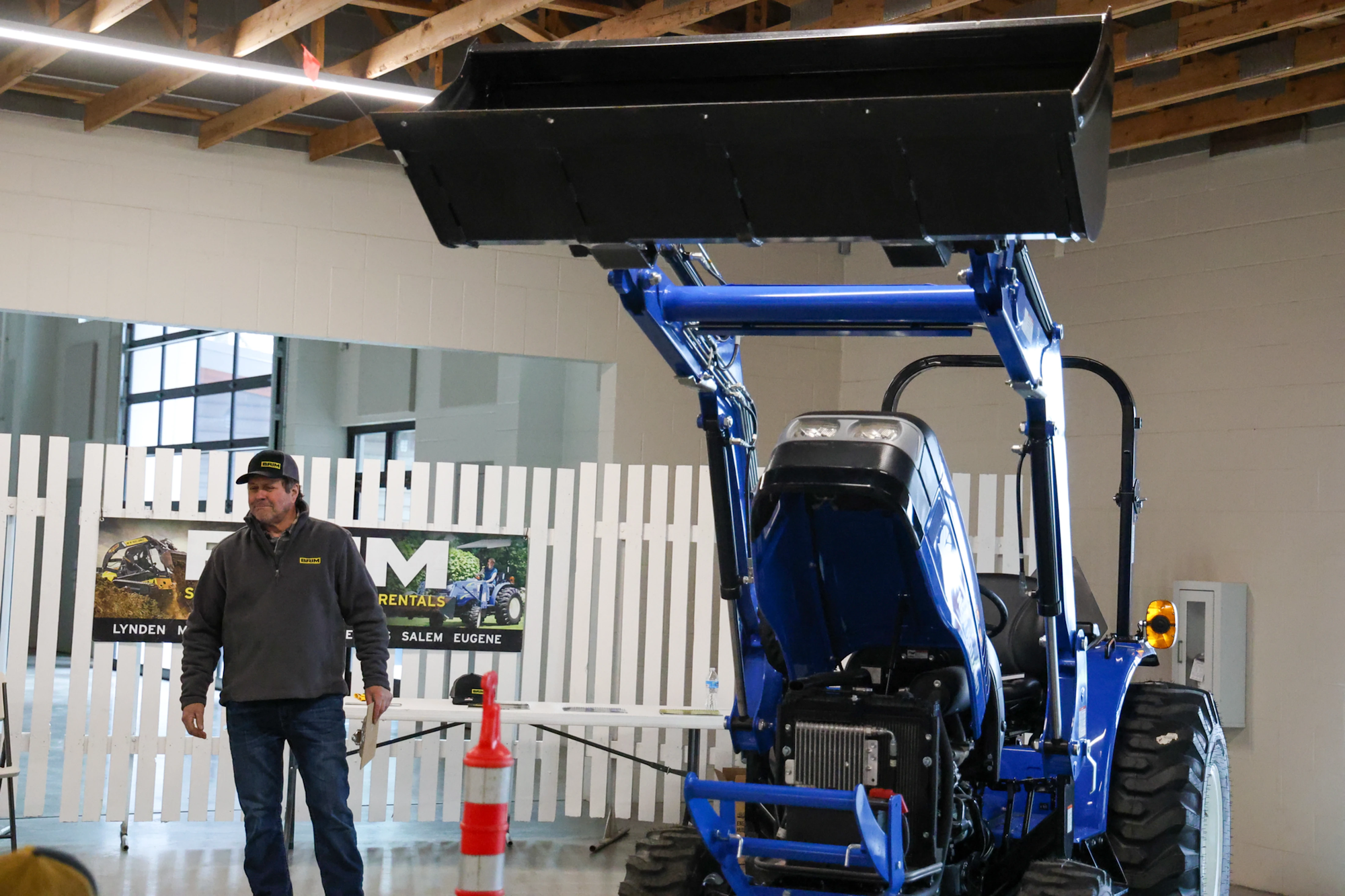 A man stands next to a blue tractor indoors, with a safety cone nearby.