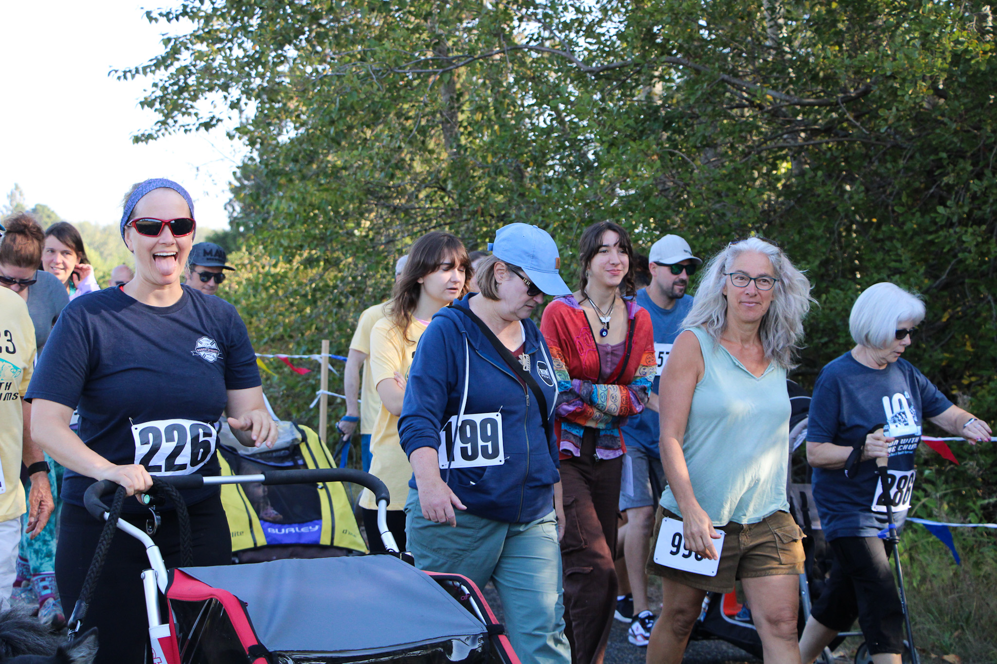 People participating in a fun run or walk event, wearing numbered bibs, with strollers in a park.