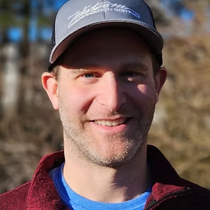 A person wearing a cap and smiling outdoors.