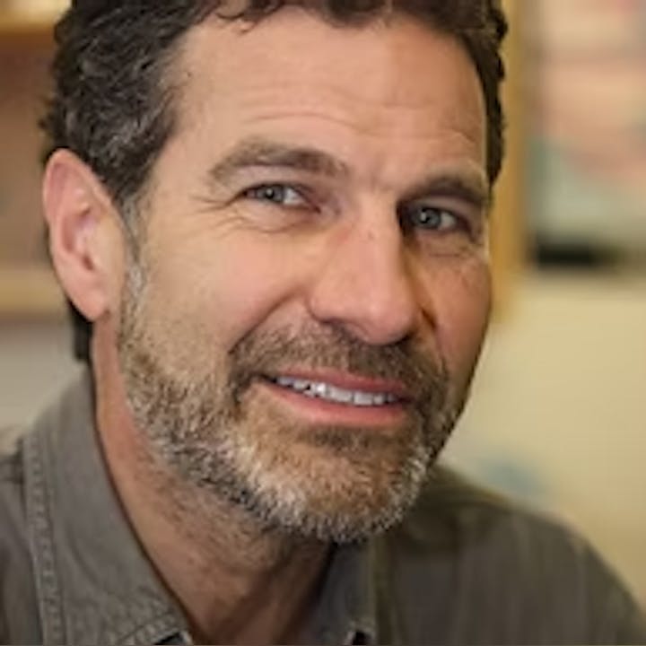 A person with a beard and gray hair, smiling slightly.