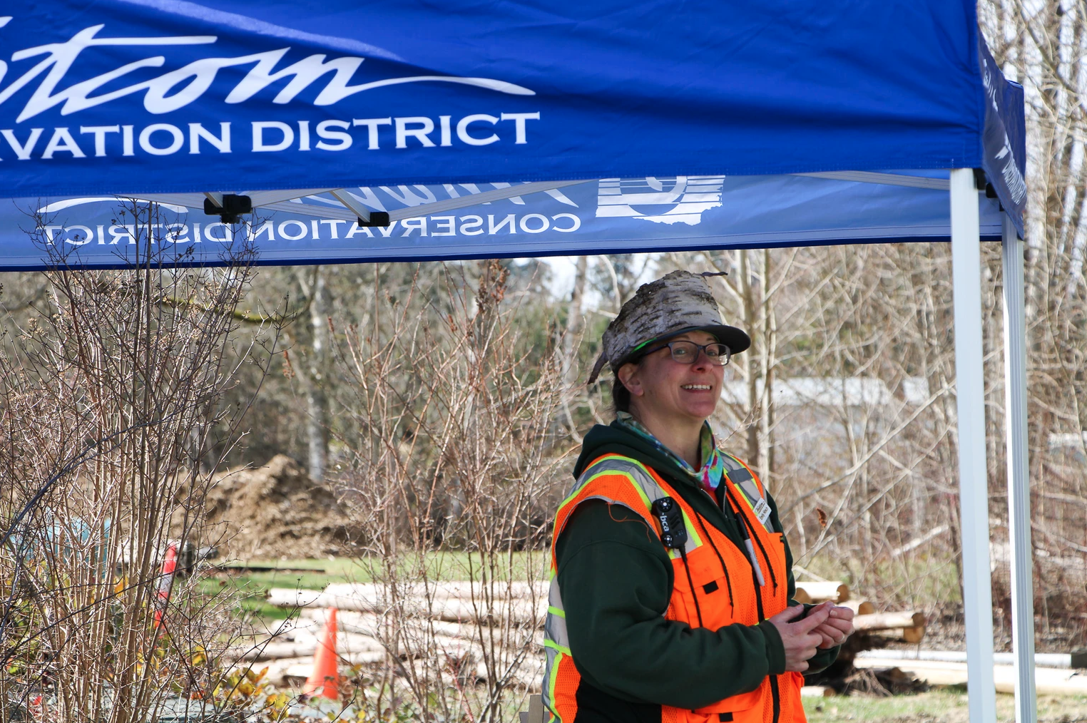 A person in a safety vest and hat smiles under a "Conservation District" tent.