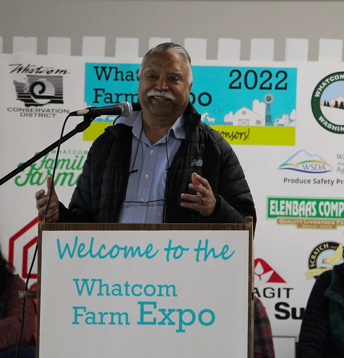 A person speaking at a podium at the Whatcom Farm Expo 2022, with event signage in the background.