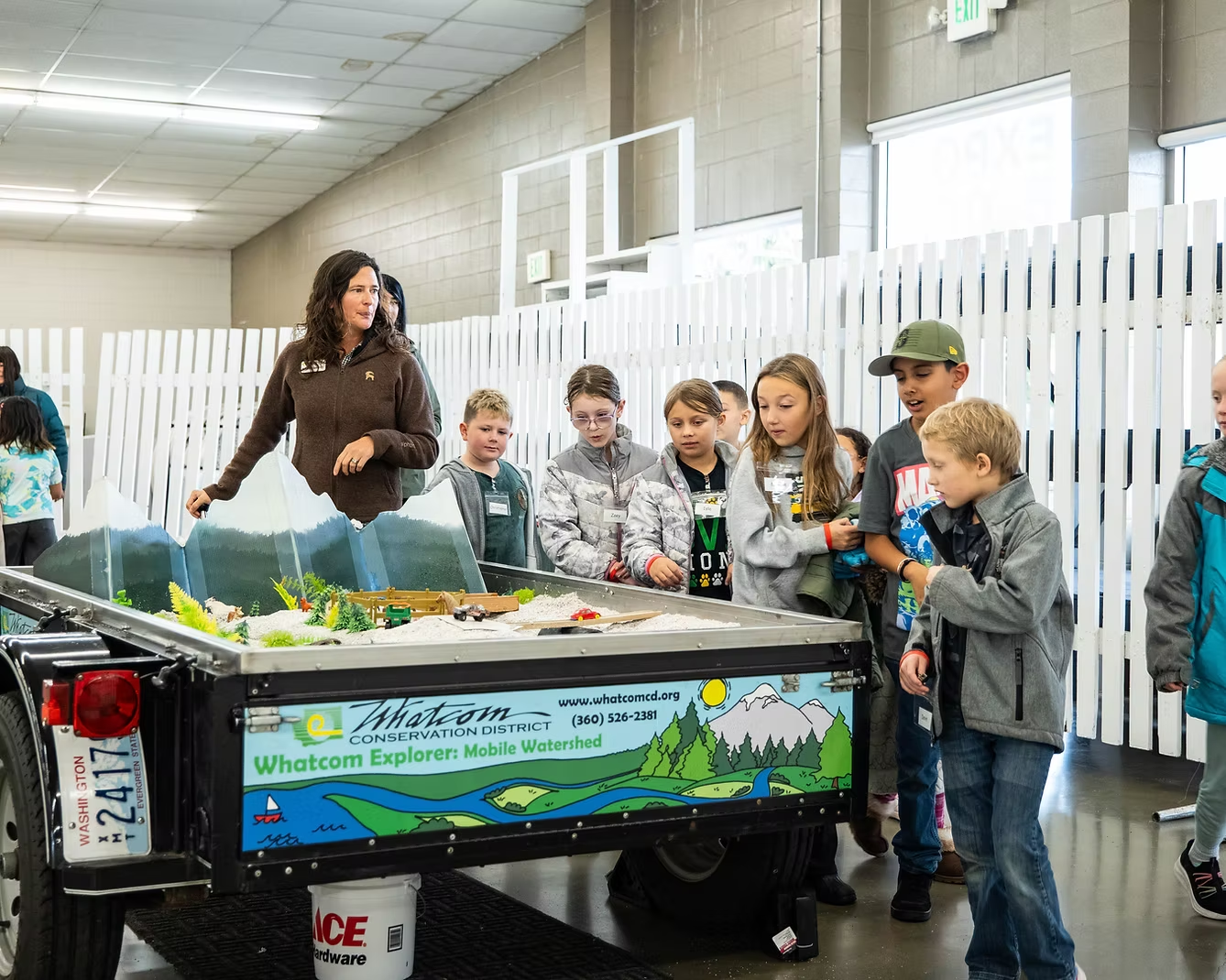 A group of children around a mobile environmental educational display by Whatcom Conservation District indoors.