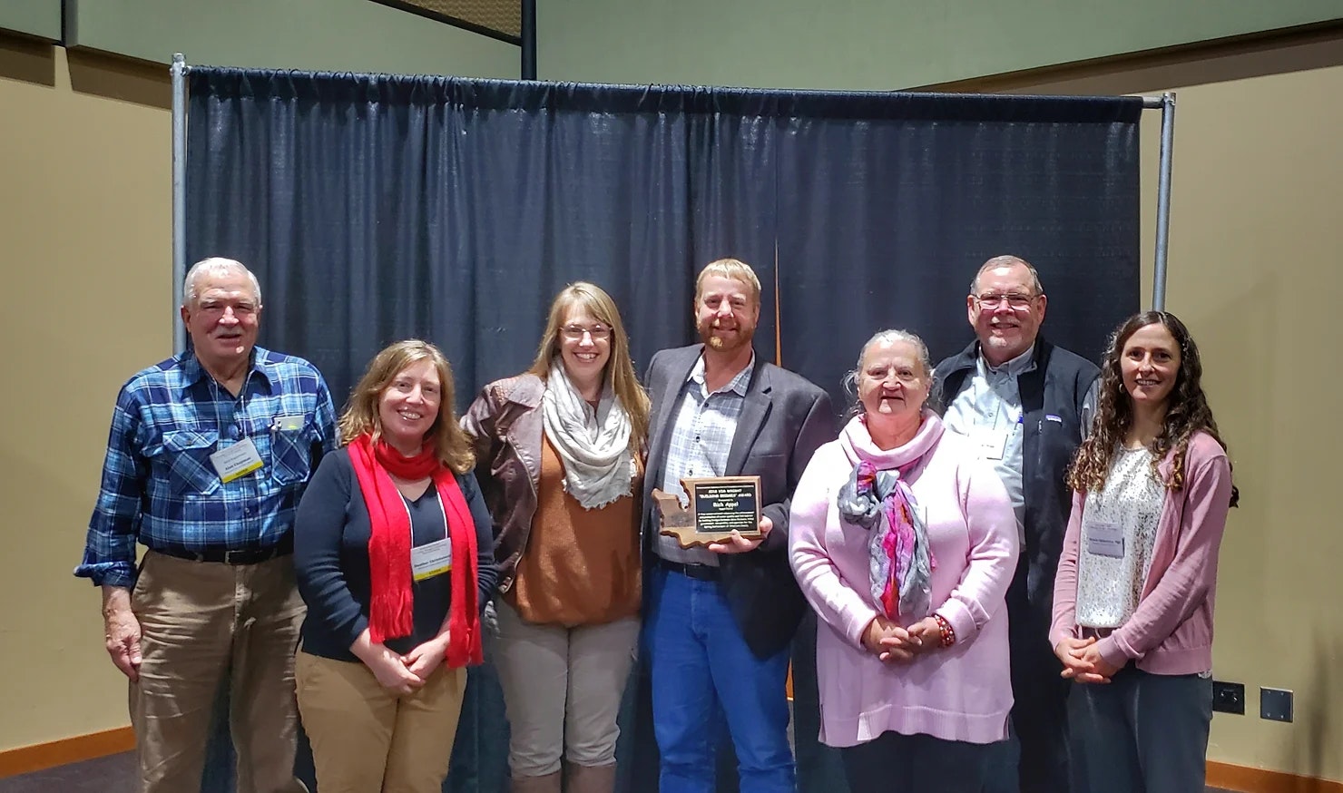 A group of seven people smiling, one holding a plaque.