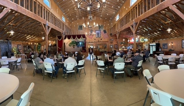 Rustic hall with people seated on folding chairs, an American flag, and a stage with a speaker.