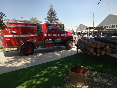 Red fire truck parked near logs and a building under clear sky.